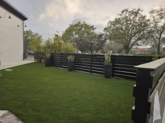 Completed artificial turf patio enclosed by a modern black wooden fence