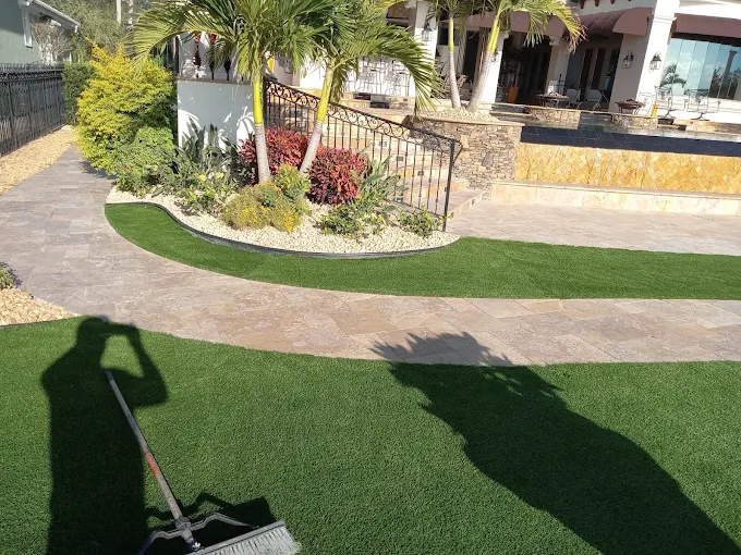 Lush tropical landscaping, artificial grass, and travertine pavers connecting outdoor living spaces