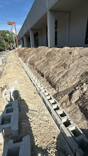 Trench and block retaining wall construction in progress along an office building facade